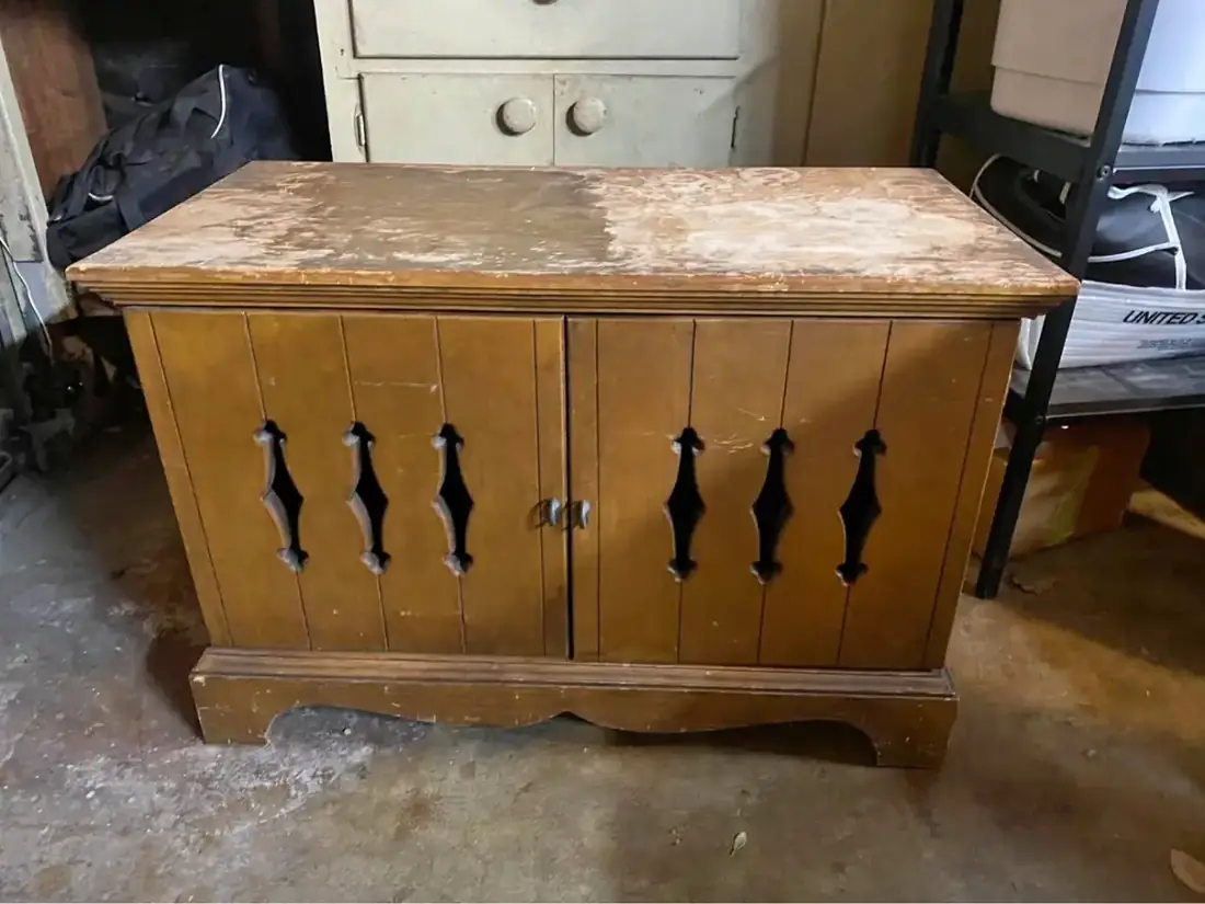 A worn orange-brown cabinet with a badly damaged top, sitting in a garage